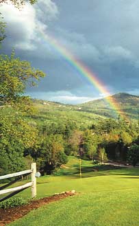 A rainbow hangs over a green field of the White Mountains